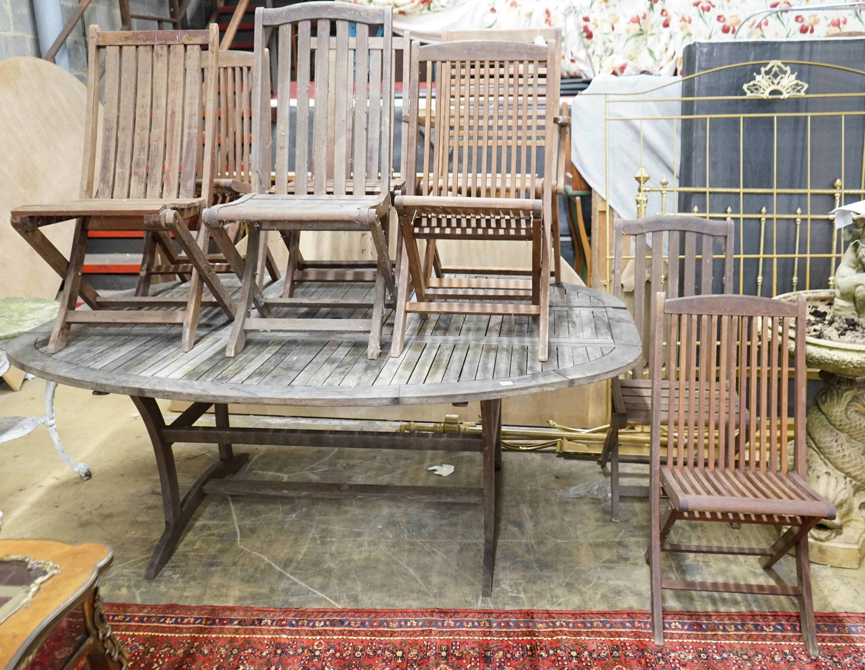 A large weathered oval teak extending garden table, length 200cm extended, height 151cm together with and eight folding teak garden chairs